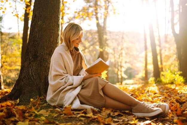 Bella giovane donna seduta su foglie d'autunno cadute in un parco a leggere un libro Relaxation