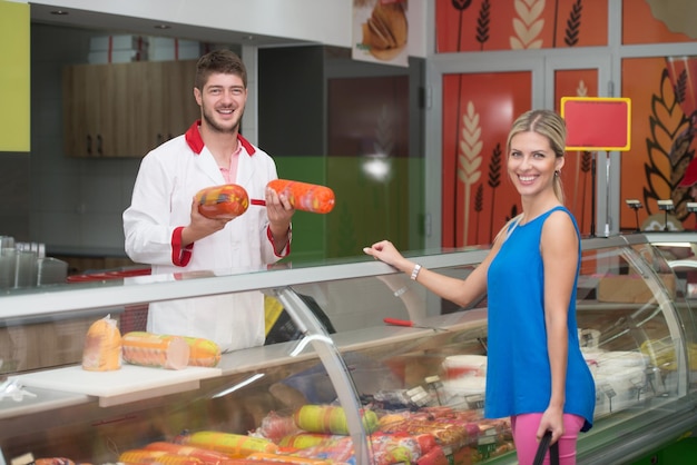 Bella giovane donna shopping per la carne nel reparto prodotti dove il venditore cerca di aiutare il suo supermercato