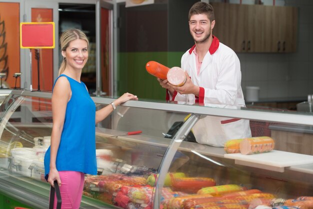 Bella giovane donna shopping per la carne nel reparto prodotti in cui il venditore cerca di aiutarla al supermercato