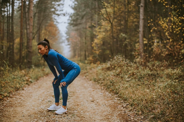 Bella giovane donna si prende una pausa durante l'esercizio all'aperto sul sentiero nel bosco in autunno