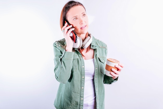 Bella giovane donna sicura di sé su sfondo bianco che indossa abiti casual e cuffie che parla al telefono su sfondo bianco