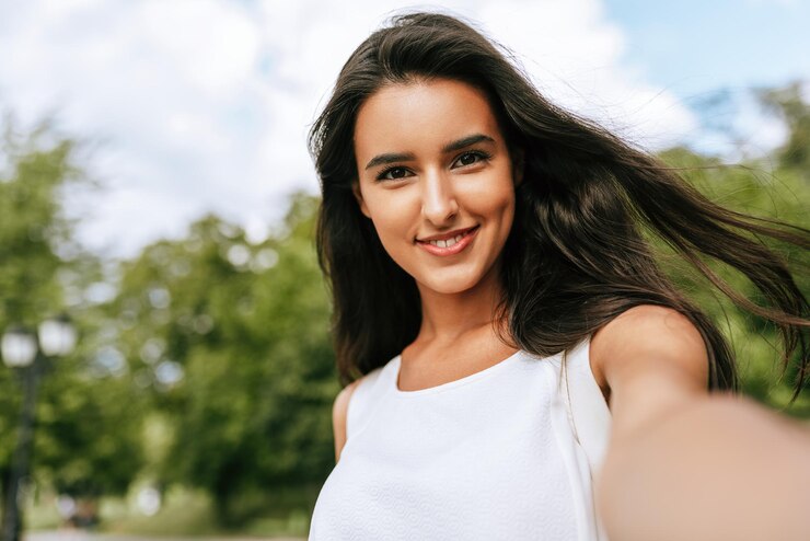 Bella giovane donna sorridente bruna che prende autoritratto sulla natura e sullo sfondo del cielo nel parco Bella donna che fa selfie sul suo dispositivo all'aperto Stile di vita e viaggi della gente