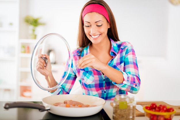 Bella giovane donna sorridente che cucina un pasto sano nella cucina domestica. Guardando il pasto.