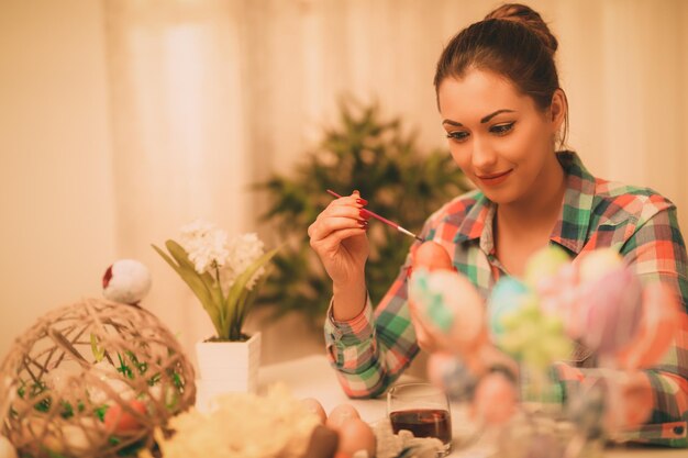 Bella giovane donna sorridente che dipinge l'uovo di Pasqua a casa.