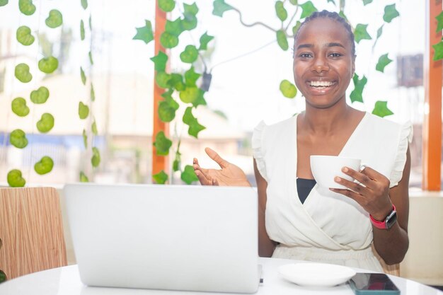 Bella giovane donna sorridente che lavora su un laptop e beve caffè seduta in un caffè