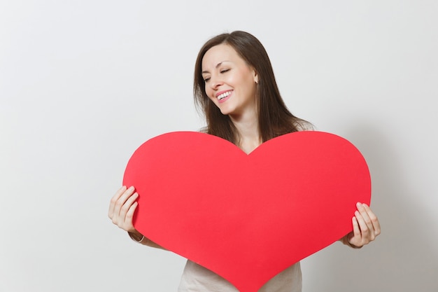 Bella giovane donna sorridente che tiene grande cuore rosso in mani isolate su fondo bianco. Copia spazio per la pubblicità. Con posto per il testo. Concetto di San Valentino o Giornata internazionale della donna.