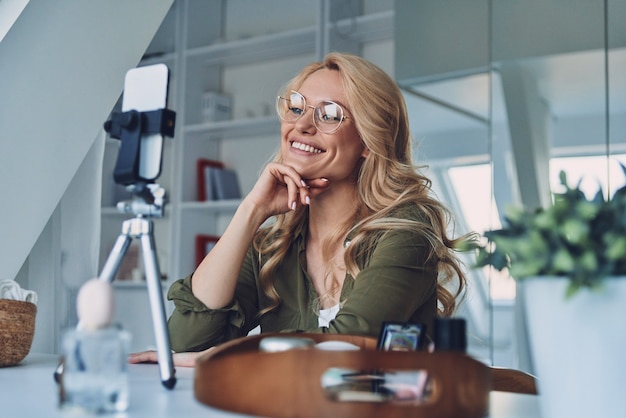 Bella giovane donna sorridente che vlogging mentre è seduta in ufficio a casa