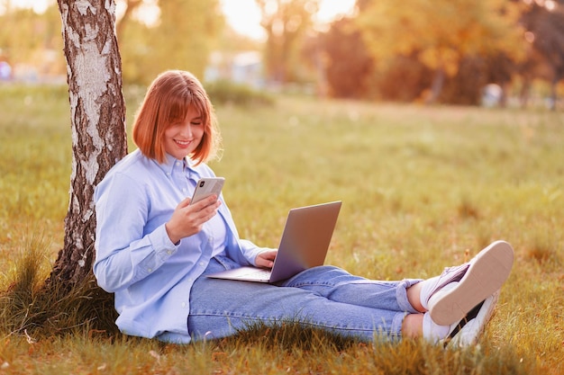 bella giovane donna sorridente con i denti seduto in un parco verde e lavorando su un computer portatile