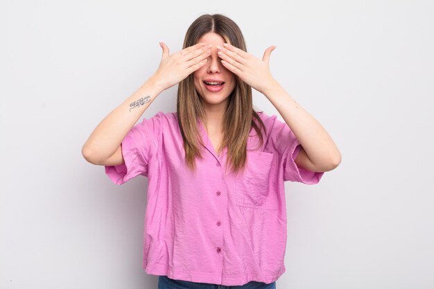 Bella giovane donna sorridente e felice, coprendosi gli occhi con entrambe le mani e aspettando un'incredibile sorpresa