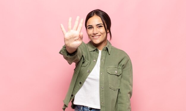 bella giovane donna sorridente e guardando amichevole, mostrando il numero quattro o quarto con la mano in avanti, conto alla rovescia