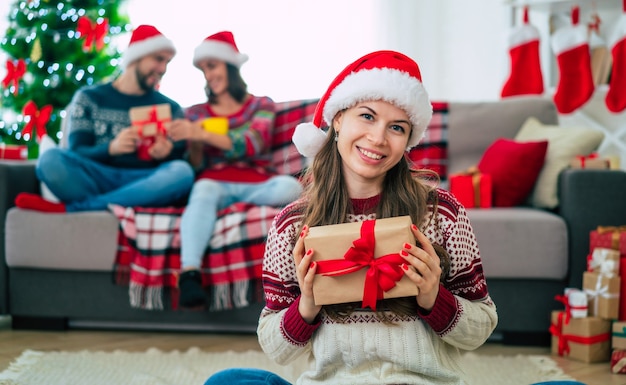 bella giovane donna sorridente felice in un maglione di Natale e cappello di Babbo Natale è in possesso di una confezione regalo