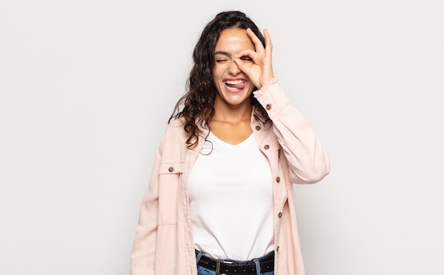 Bella giovane donna sorridente felicemente con una faccia buffa, scherzando e guardando attraverso lo spioncino, spiando i segreti