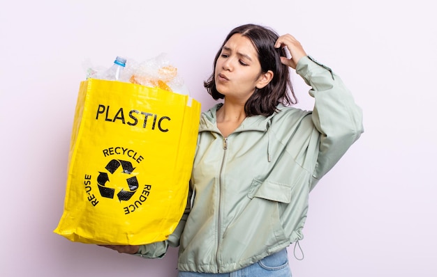 Bella giovane donna sorridente felicemente e sognare ad occhi aperti o dubitare del concetto di riciclaggio della plastica