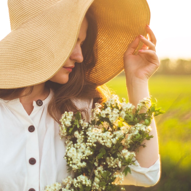 Bella giovane donna sorridente in abito vintage e cappello di paglia in fiori di campo di campo. La ragazza tiene in mano un cesto di fiori