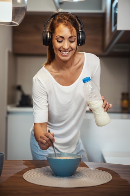 Bella giovane donna sorridente sta preparando la sua sana colazione nella sua cucina e ascolta musica.