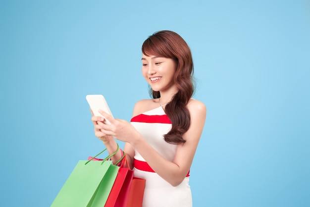 Bella giovane donna sta usando uno smartphone per lo shopping online isolato su sfondo blu studio