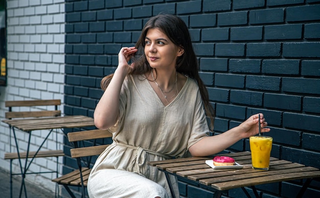 Bella giovane donna sulla terrazza del caffè con succo e ciambella