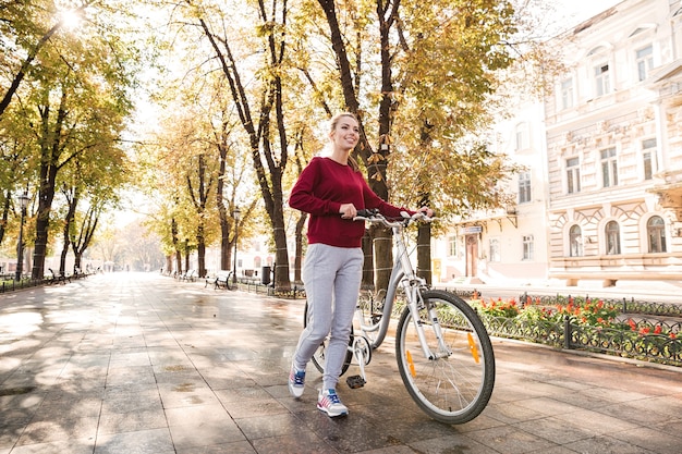 Bella giovane donna vestita di maglione che cammina con la sua bicicletta in città