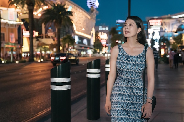 Bella giovane donna viaggiatore che cammina nella città di notte a las vegas nevada. allegra signora turistica che visita la città con vita notturna. la donna in abito sorridente si rilassa in un'area moderna e trafficata negli Stati Uniti.