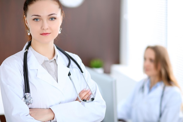 Bella giovane dottoressa sorridente in piedi in un ospedale con il suo collega in background.