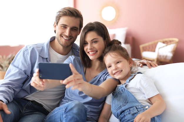 Bella giovane famiglia con un bambino che si fa un selfie con uno smartphone a casa sul divano.