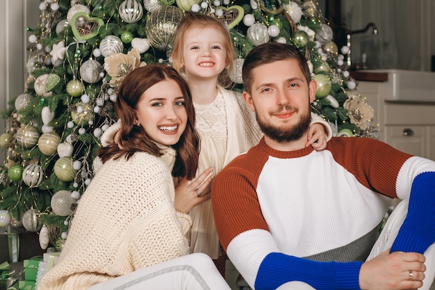 Bella giovane famiglia seduta accanto a un albero di Natale ben decorato