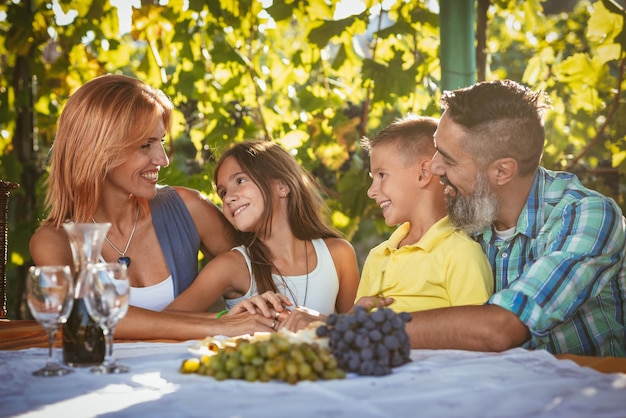 Bella giovane famiglia sorridente di quattro persone che fa picnic in una vigna.