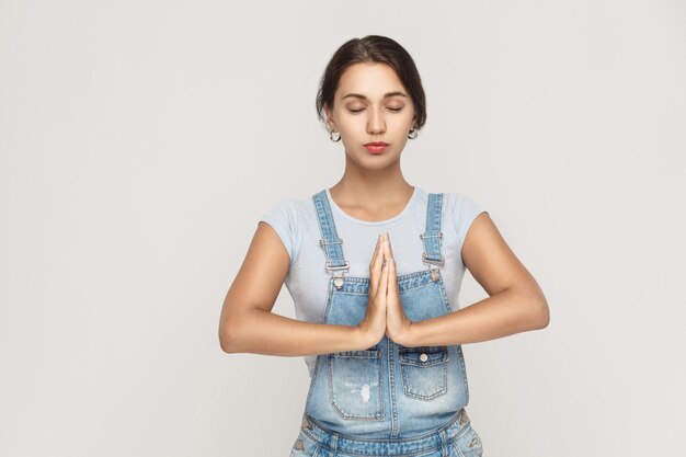 Bella giovane femmina caucasica, tenendosi per mano in namaste o in preghiera, tenendo gli occhi chiusi mentre praticava lo yoga e meditava a casa da solo. Studio girato su sfondo grigio.