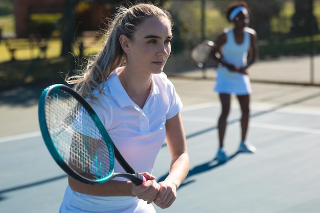 Bella giovane giocatrice caucasica femminile con partner afroamericano al campo da tennis