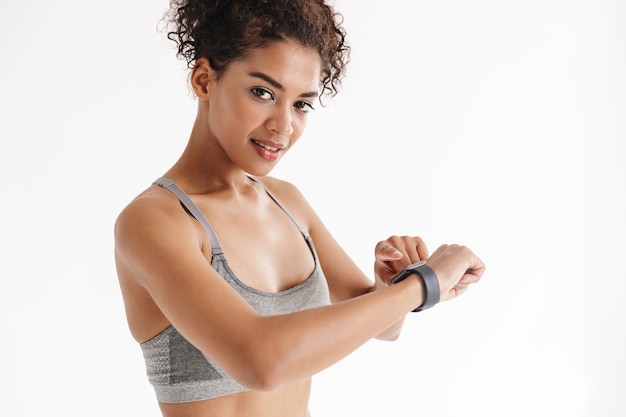 bella giovane incredibile fitness sportivo donna africana in posa isolato sul muro bianco utilizzando orologio orologio.