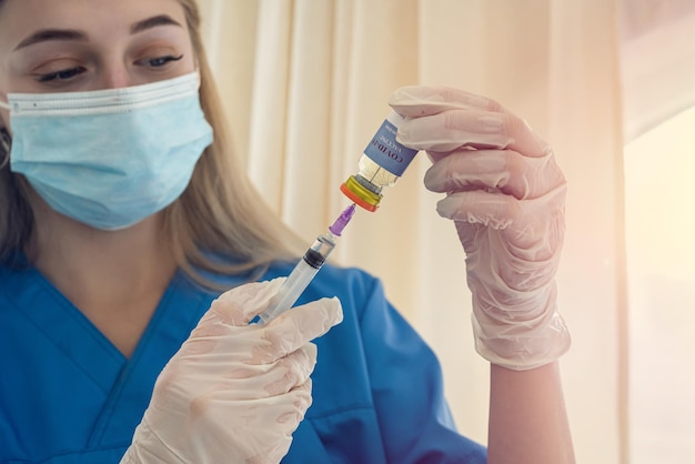 Bella giovane infermiera bionda con maschera e guanti compone un vaccino per un paziente Concetto di medicina