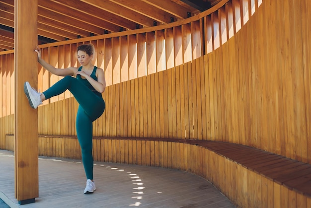 Bella giovane istruttrice di fitness dà lezioni in video utilizzando il computer portatile su una veranda in legno sulla strada