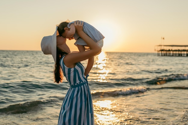 Bella giovane madre bacio figlia al mare tramonto e sfondo spiaggia Felice vacanza in famiglia Viaggi Caucasica donna felice con bambino fuori al tramonto sull'oceano Maternità amore cura Silhouette