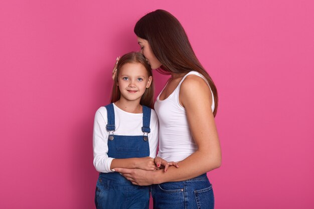 Bella giovane madre che abbraccia il suo bambino e bacia teneramente sua figlia sulla testa.