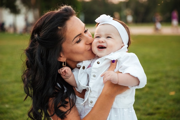 Bella giovane madre che bacia la sua piccola figlia nel parco