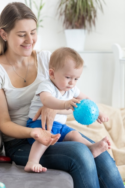 Bella giovane madre che gioca con il suo bambino sul divano con la palla