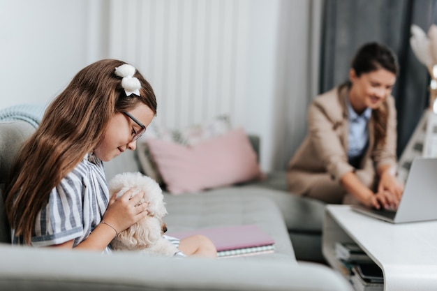 Bella giovane madre che lavora da casa mentre sua figlia guarda la lezione di scuola online. Distanziamento sociale e stile di vita Covid-19 o Coronavirus.