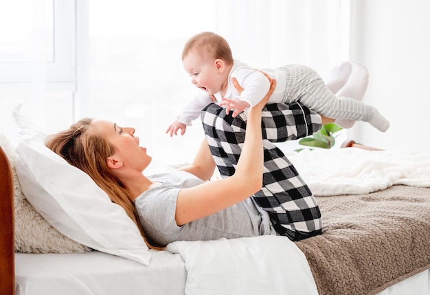 Bella giovane madre che tiene il piccolo neonato sulle gambe e guarda il bambino. Bella ragazza che gioca con il figlio bambino nel letto al mattino. Momenti felici in famiglia