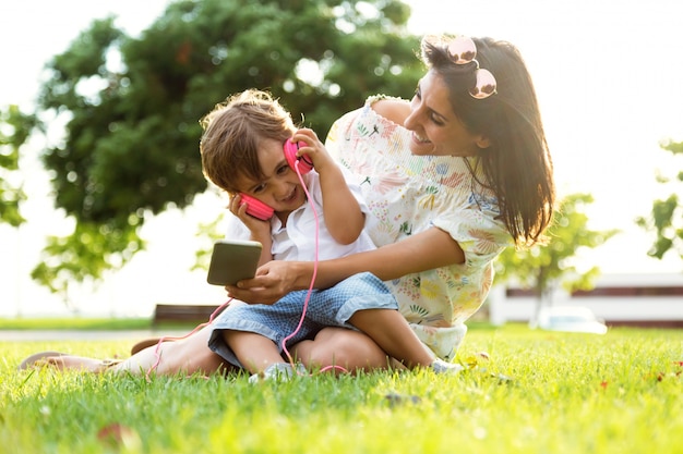 Bella giovane madre con il figlio ad ascoltare musica nel parco.