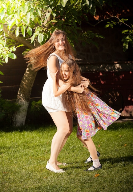 Bella giovane madre e figlia che ballano sull'erba in cortile