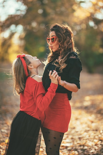 Bella giovane madre e sua figlia felice che si divertono nella foresta al tramonto. Si abbracciano, sorridono e si guardano.