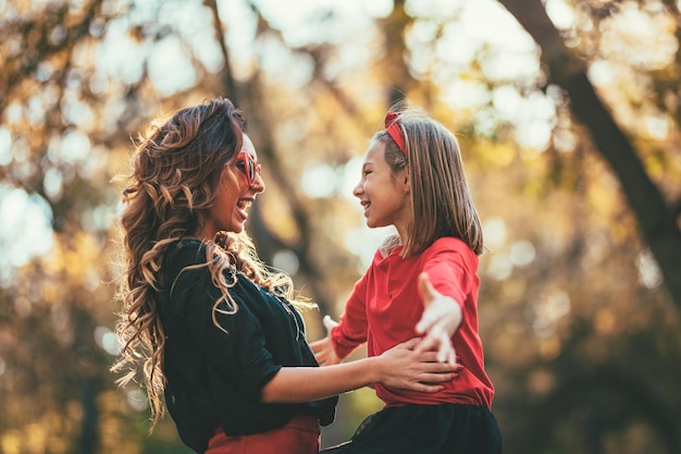 Bella giovane madre e sua figlia felice che si divertono nella foresta al tramonto. Si abbracciano, sorridono e si guardano.