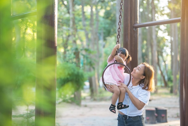 Bella giovane madre gioca con tua figlia divertendoti nel parco giochi con una luce flairBuon giorno della mammaGente della Thailandia