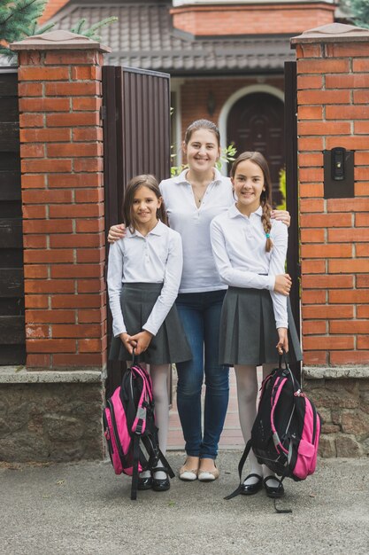 Bella giovane madre in piedi sulla porta con due figlie in partenza per la scuola
