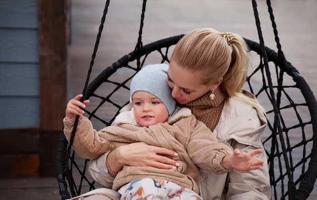 Bella giovane mamma e bambino che si abbracciano e si divertono. Madre che tiene suo figlio. Modelli che indossano maglione beige lavorato a maglia, giacca, berretto. Ritratto di stile di vita