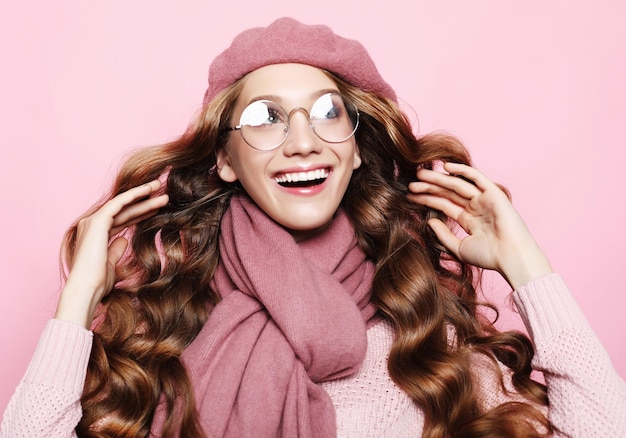 Bella giovane modella con lunghi capelli ondulati che indossa una sciarpa berretto rosa e occhiali da vista