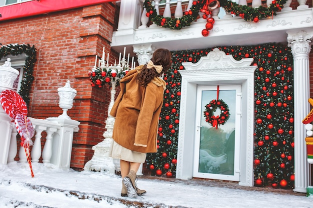 Bella giovane ragazza adulta allegra e felice sotto il portico della casa vicino alla porta a Natale