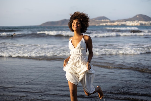 Bella giovane ragazza africana nera che corre felicemente sulla spiaggia