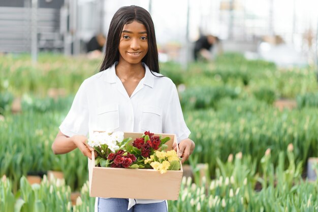 Bella giovane ragazza afroamericana sorridente, lavoratore con fiori in serra.