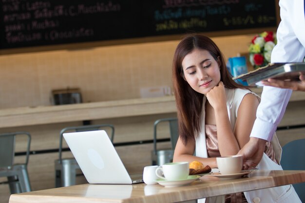 Bella giovane ragazza asiatica che lavora in una caffetteria con un computer portatile